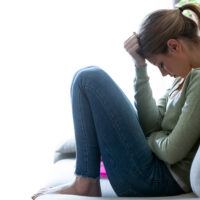 Emotionally distressed woman crouched with hand on head on sofa Emotionally distressed woman crouched with hand on head on sofa