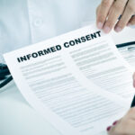 young woman signing an informed consent form handed by doctor