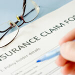 person filling out insurance claim form with glasses on table