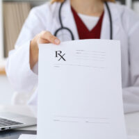 Female doctor hands prescription to patient closeup