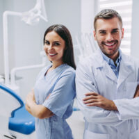 smiling doctor and assistant with crossed arms at dental clinic