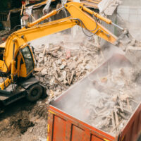 Excavator breaks building and loads construction waste into truck with its bucket. Demolition of building.