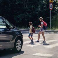 Car in front of children on pedestrian crossing walking from the school and looking at their smartphones