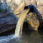 Wastewater sewage pipe dumps the dirty contaminated water into the river. Water pollution, environment contamination concept