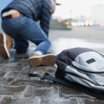 Backpack lying on slippery paving slabs near falling man closeup. Ice injuries concept