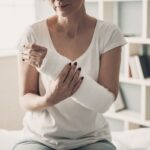 Close-up of Female Broken Arm in Plaster Cast. Caucasian Injured Woman in White T-Shirt Sitting and Holding Wrist in Gypsum Bandage with Physical Pain in Fractured Bone. Health Care concept