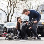 Reliable young man helping an injured woman while waiting for the ambulance after bicycle accident on city street Reliable young man helping an injured woman while waiting for the ambulance after bicycle accident on city street