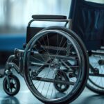 A close-up of a wheelchair with shiny wheels and a dark blue seat, set against a softly lit room with blurred furniture in the background. A close-up of a wheelchair with shiny wheels and a dark blue seat, set against a softly lit room with blurred furniture in the background.
