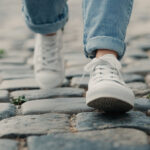 Close-up of a woman’s feet in casual sneakers jeans stumbling on uneven paving slabs during a walk, highlighting the risks of accidents and injuries caused by poorly maintained urban infrastructure Close-up of a woman’s feet in casual sneakers jeans stumbling on uneven paving slabs during a walk, highlighting the risks of accidents and injuries caused by poorly maintained urban infrastructure