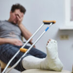 A sad man with a broken leg sits on a chair.