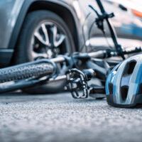 A bicycle rests on the asphalt after colliding with an SUV, showcasing a blue helmet beside it and a traffic signal in the background, captured in vivid detail.