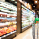 woman hand hold supermarket shopping cart with abstract blur organic fresh fruits and vegetable on shelves in grocery store defocused woman hand hold supermarket shopping cart with abstract blur organic fresh fruits and vegetable on shelves in grocery store defocused
