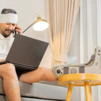 Person recovery from accident fracture broken bone injury with leg and head, support wrist while work with laptop and phone. Social security and health insurance concept. Person recovery from accident fracture broken bone injury with leg and head, support wrist while work with laptop and phone. Social security and health insurance concept.