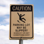 Caution, Slippery when wet sign in a parking lot. Warning patrons. Blue sky with fluffy white clouds in background