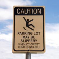 Caution, Slippery when wet sign in a parking lot. Warning patrons. Blue sky with fluffy white clouds in background Caution, Slippery when wet sign in a parking lot. Warning patrons. Blue sky with fluffy white clouds in background