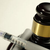 Close-up of semaglutide syringe placed near a wooden judge’s gavel with a golden band. Concept of legal regulation of diabetes treatment, weight loss medications, pharmaceutical law