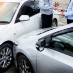 Insurance agent writing on clipboard while examining car after accident claim being assessed and processed