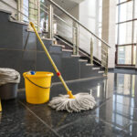 Wet floor caution sign and cleaning equipment in modern building hallway with natural light