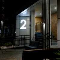 Street entrance to an apartment building with landscaping elements. A luminous number above the entrance to a modern residential complex at night. Street entrance to an apartment building with landscaping elements. A luminous number above the entrance to a modern residential complex at night.