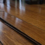 Close-up of a wooden floor with visible warping and gaps between planks. The image conveys neglect and potential tripping hazards in the home.