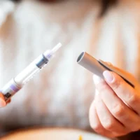 Close-up of hands holding an insulin pen and cap. The person wears a cream sweater, evoking a calm, focused moment, possibly preparing for an injection.