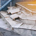 Poor construction of concrete steps on the porch. Damaged concrete front steps with broken tiles. Broken tiled front porch stairs, damaged steps need renovation closeup. Selective focus.