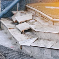 Poor construction of concrete steps on the porch. Damaged concrete front steps with broken tiles. Broken tiled front porch stairs, damaged steps need renovation closeup. Selective focus.
