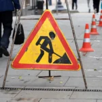 Road works sign, street repairs. Orange roadblock cones on sidewalk in city