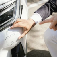 Insurance agents assist clients in an outdoor setting after a car accident, inspecting the vehicle for damage, discussing policy coverage, repair options, liability, and pursuing a claim.